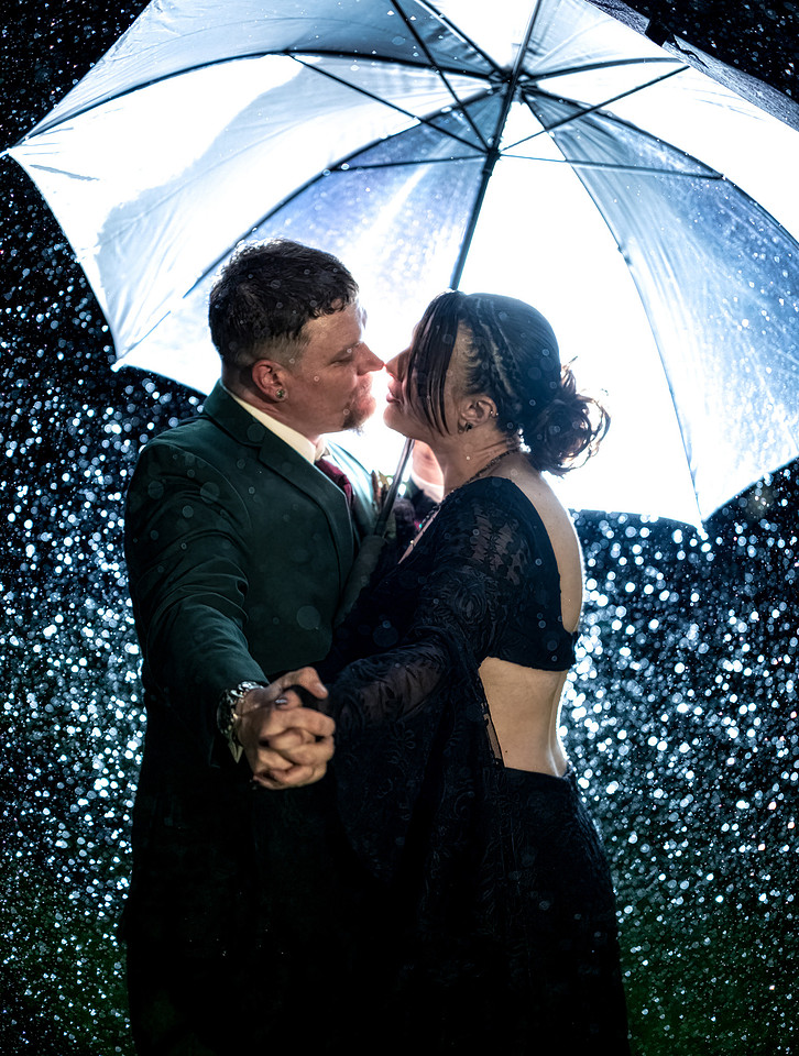 Newlyweds kissing beneath an umbrella in the rain