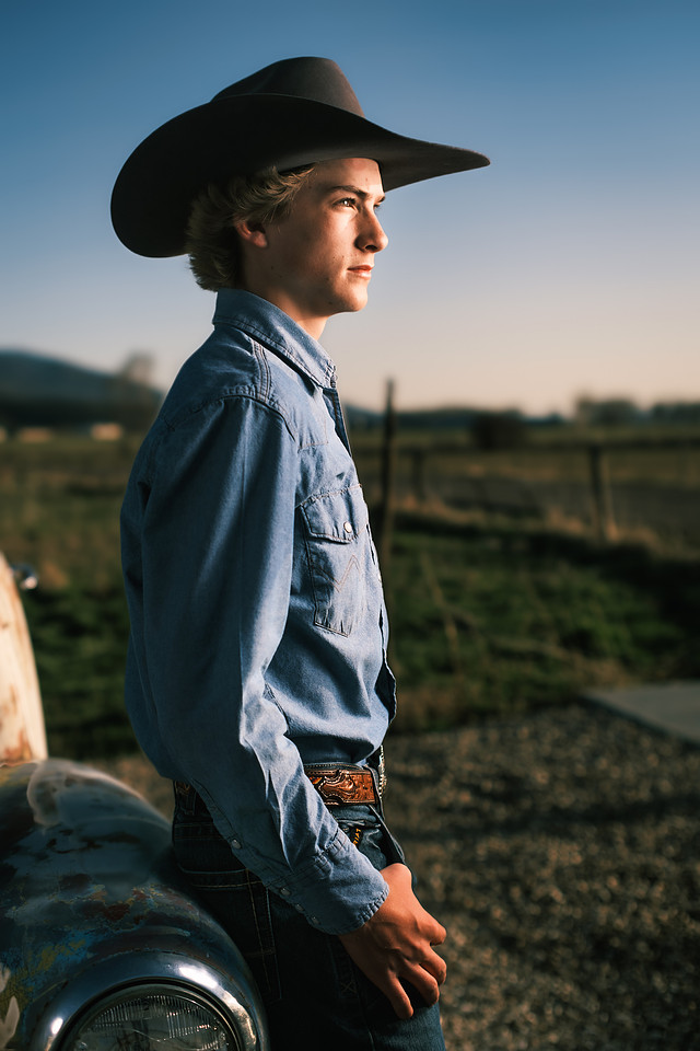 A young man in a cowboy hat photographed beside an old vehicle